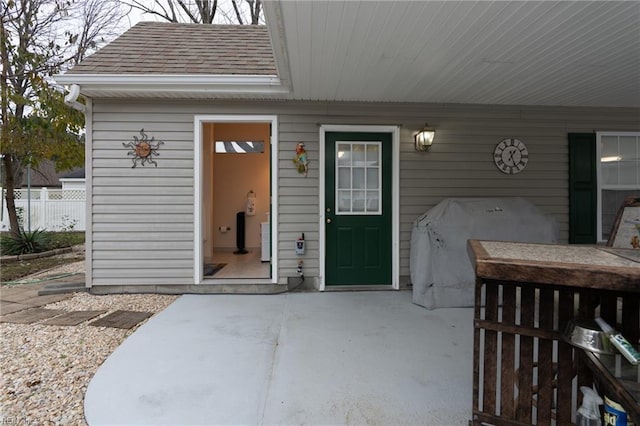 doorway to property with a patio area, a shingled roof, and fence