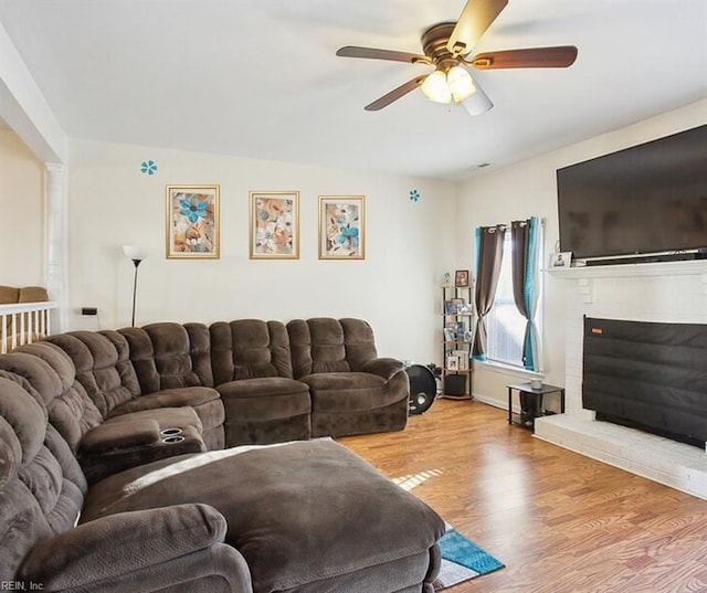 living area featuring a brick fireplace, wood finished floors, and a ceiling fan