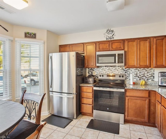 kitchen featuring brown cabinets, light stone counters, backsplash, stainless steel appliances, and light tile patterned floors