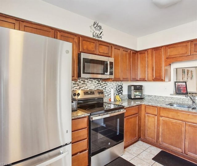 kitchen with light tile patterned flooring, light stone countertops, stainless steel appliances, and a sink