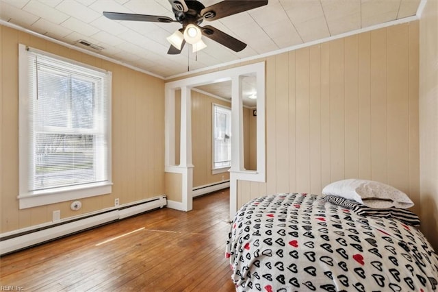 bedroom with a baseboard heating unit, ornamental molding, baseboard heating, hardwood / wood-style flooring, and a ceiling fan