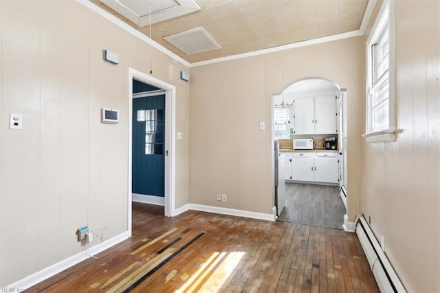 spare room featuring attic access, ornamental molding, baseboard heating, arched walkways, and dark wood-style flooring