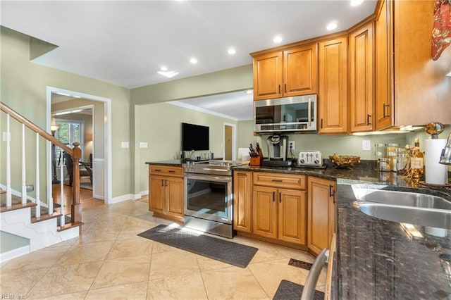 kitchen featuring baseboards, dark stone counters, a sink, appliances with stainless steel finishes, and brown cabinets