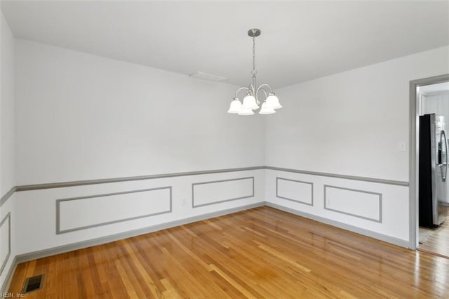 unfurnished dining area with a decorative wall, light wood-style floors, visible vents, and a chandelier