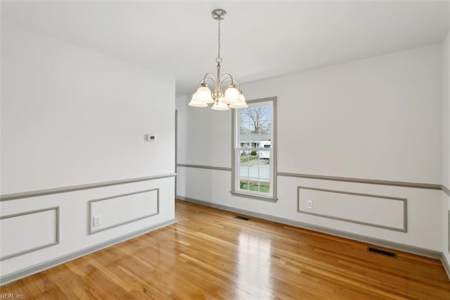 spare room featuring visible vents, baseboards, light wood-style floors, and a notable chandelier