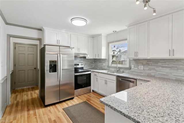 kitchen with under cabinet range hood, light stone counters, appliances with stainless steel finishes, white cabinetry, and a sink