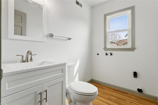 half bathroom featuring vanity, wood finished floors, visible vents, baseboards, and toilet