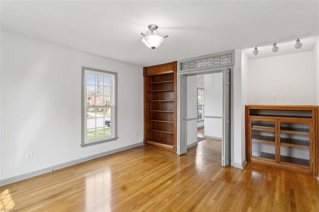 unfurnished bedroom featuring light wood-type flooring, baseboards, and rail lighting