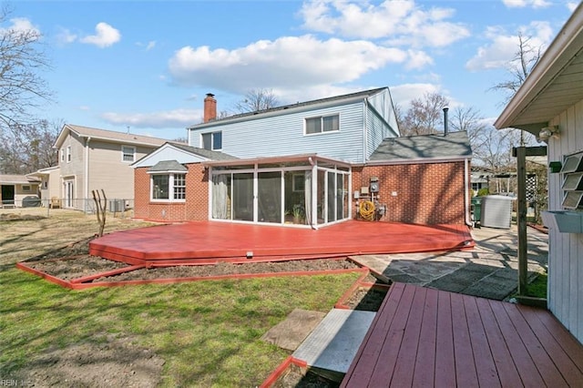 back of property featuring a yard, brick siding, a sunroom, and a wooden deck