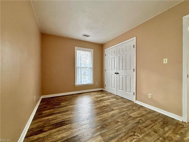 unfurnished bedroom featuring visible vents, baseboards, a closet, and wood finished floors