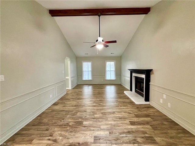 unfurnished living room with wainscoting, wood finished floors, a fireplace with raised hearth, and a ceiling fan