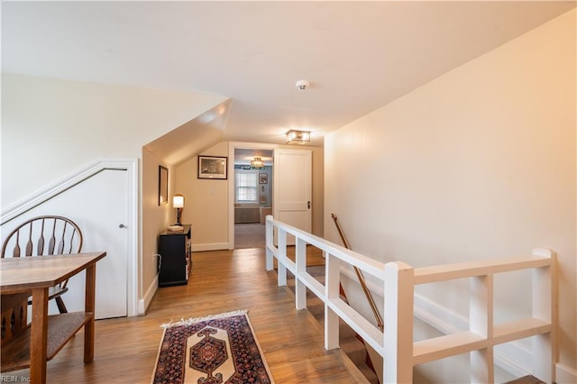 hall with baseboards, an upstairs landing, lofted ceiling, and wood finished floors