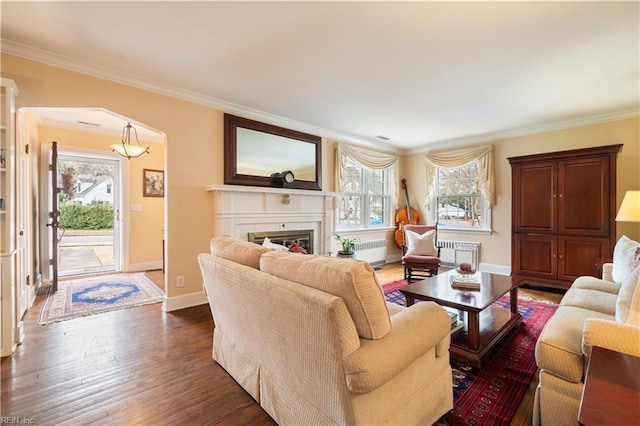 living area featuring radiator heating unit, arched walkways, ornamental molding, a tile fireplace, and dark wood-type flooring