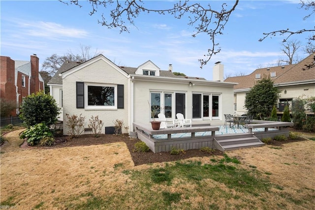 rear view of house featuring a chimney, a lawn, brick siding, and a wooden deck