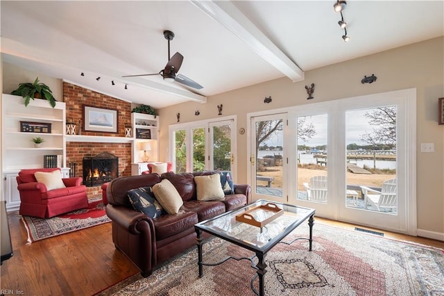 living room featuring visible vents, vaulted ceiling with beams, a fireplace, wood finished floors, and a ceiling fan