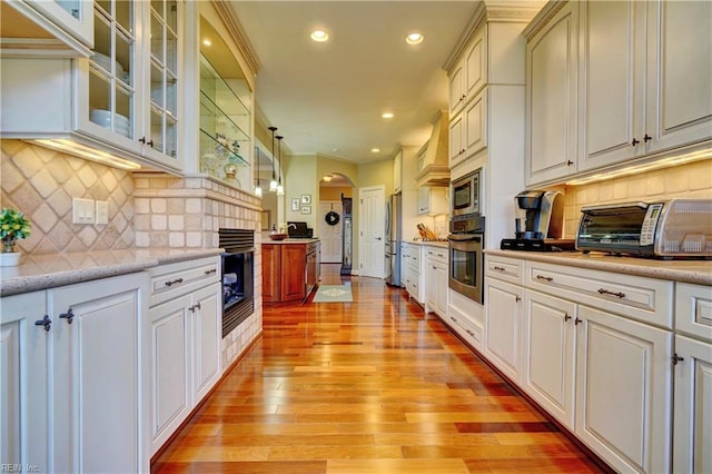 kitchen featuring glass insert cabinets, recessed lighting, light wood-style flooring, appliances with stainless steel finishes, and arched walkways