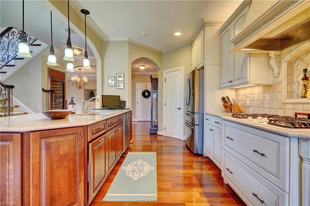 kitchen featuring a chandelier, custom range hood, wood finished floors, arched walkways, and stainless steel appliances