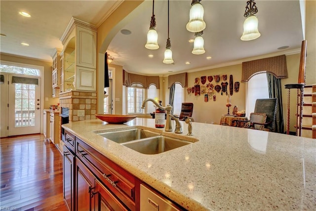 kitchen with wood finished floors, light stone countertops, arched walkways, a sink, and crown molding