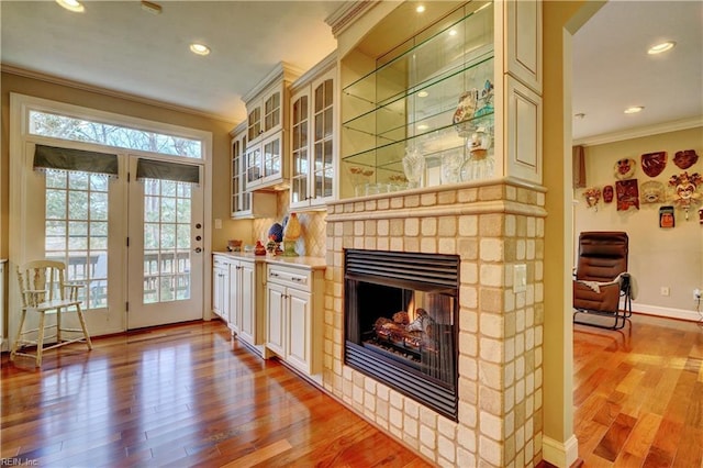 bar featuring a glass covered fireplace, baseboards, light wood-style floors, and ornamental molding