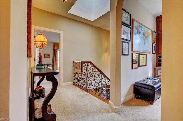 hall featuring baseboards, an upstairs landing, carpet, and a skylight