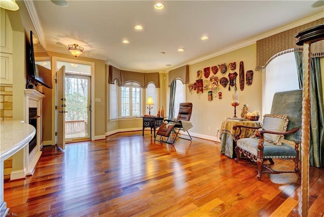 sitting room with wood finished floors, baseboards, a fireplace, recessed lighting, and ornamental molding