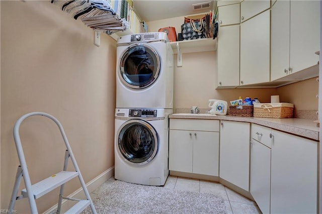 laundry area with visible vents, stacked washer and dryer, cabinet space, light tile patterned floors, and baseboards