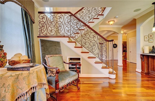 stairway with wood finished floors, arched walkways, ornamental molding, and ornate columns