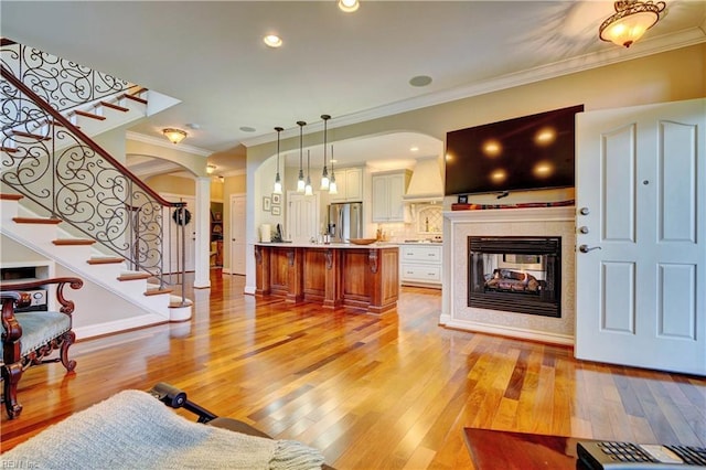 living area featuring arched walkways, light wood-style flooring, crown molding, and decorative columns