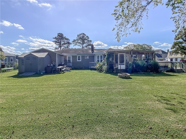 back of property featuring a shed, an outdoor fire pit, a deck, a sunroom, and an outbuilding