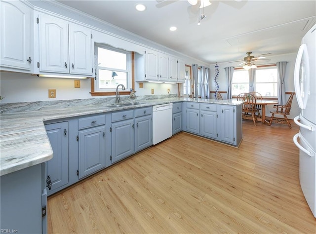 kitchen featuring light wood finished floors, a peninsula, white appliances, white cabinetry, and a sink