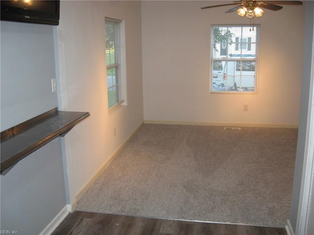 unfurnished room featuring dark wood finished floors, baseboards, dark carpet, and ceiling fan