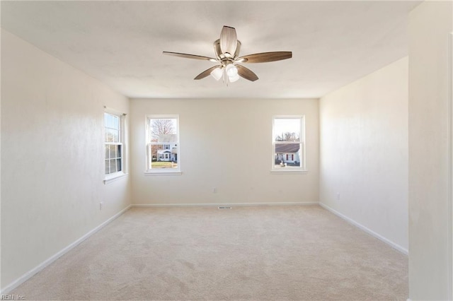 spare room featuring a ceiling fan, light colored carpet, and baseboards