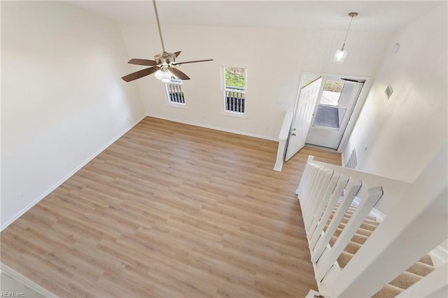 unfurnished living room featuring a wealth of natural light, baseboards, light wood-style floors, and stairs