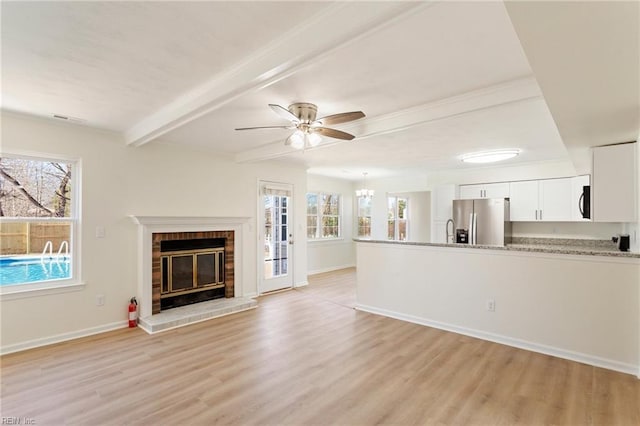 unfurnished living room featuring beamed ceiling, light wood-style floors, a healthy amount of sunlight, and a fireplace