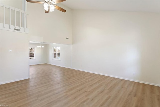 empty room featuring baseboards, light wood-style floors, high vaulted ceiling, and ceiling fan with notable chandelier