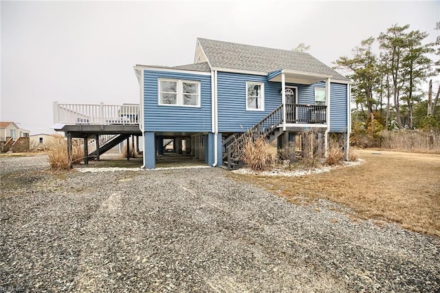 coastal inspired home featuring a carport, gravel driveway, stairs, and a shingled roof