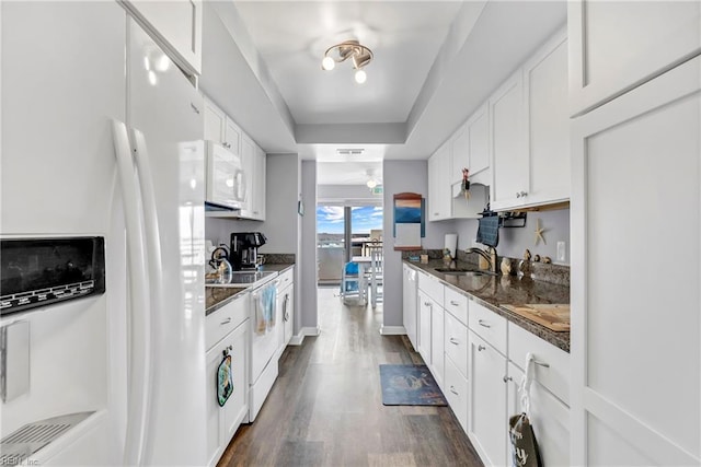 kitchen with a tray ceiling, dark wood-style floors, white cabinets, white appliances, and a sink