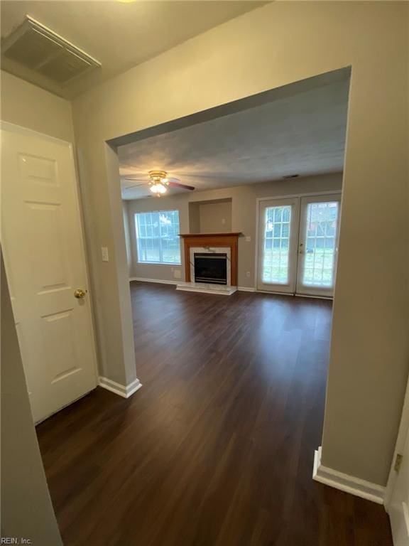 unfurnished living room with visible vents, dark wood-type flooring, a fireplace with raised hearth, baseboards, and ceiling fan