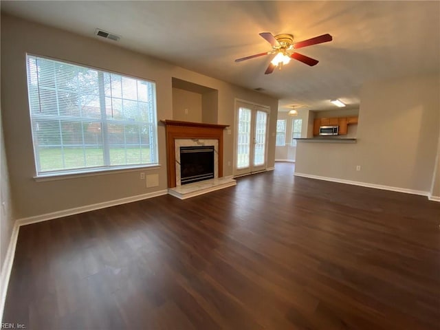 unfurnished living room featuring visible vents, a ceiling fan, dark wood-style floors, a premium fireplace, and baseboards