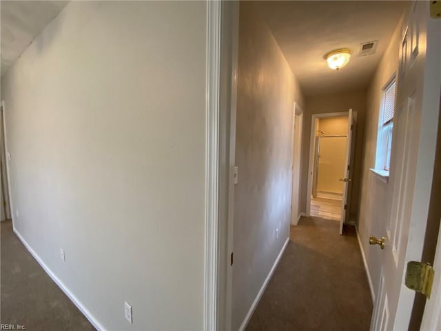 hall with dark colored carpet, visible vents, and baseboards