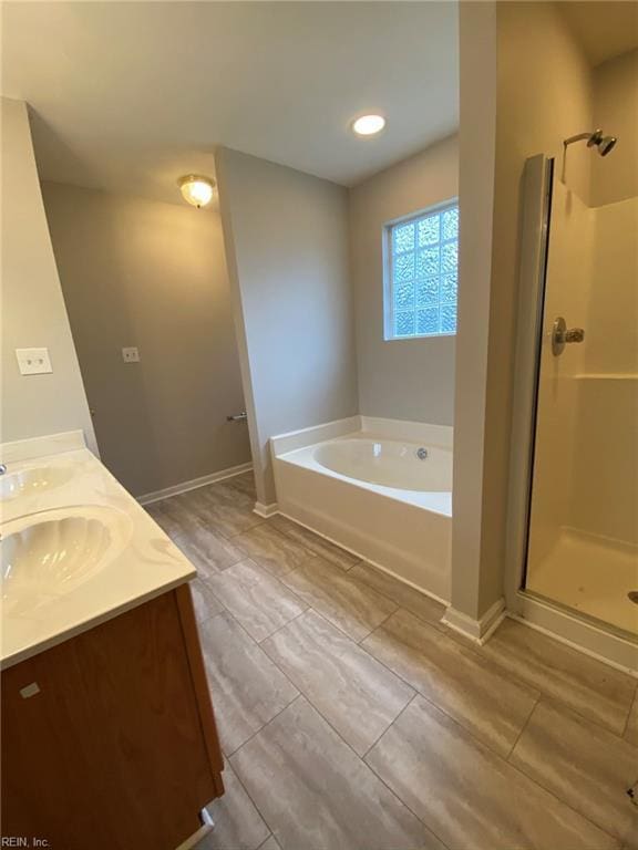 bathroom with a bath, a shower stall, baseboards, and double vanity