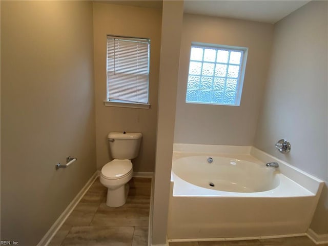 full bathroom featuring a bath, tile patterned flooring, toilet, and baseboards