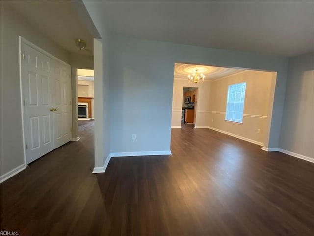 spare room with dark wood-style floors, baseboards, a fireplace with raised hearth, and a chandelier