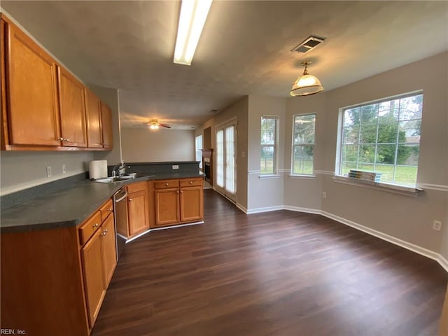 kitchen featuring dark countertops, dark wood-type flooring, a peninsula, brown cabinetry, and stainless steel dishwasher