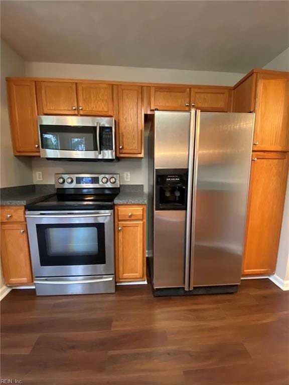 kitchen featuring dark wood finished floors, brown cabinetry, appliances with stainless steel finishes, and dark countertops