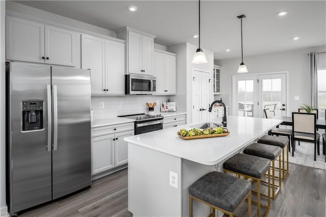 kitchen with a kitchen island with sink, a sink, backsplash, stainless steel appliances, and light countertops