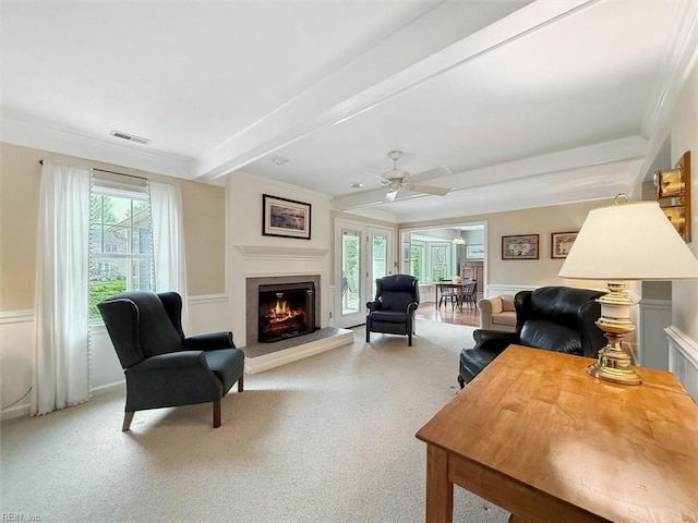 carpeted living room featuring visible vents, a fireplace, ornamental molding, ceiling fan, and beamed ceiling