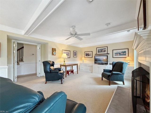 living area featuring beam ceiling, carpet flooring, wainscoting, and a ceiling fan