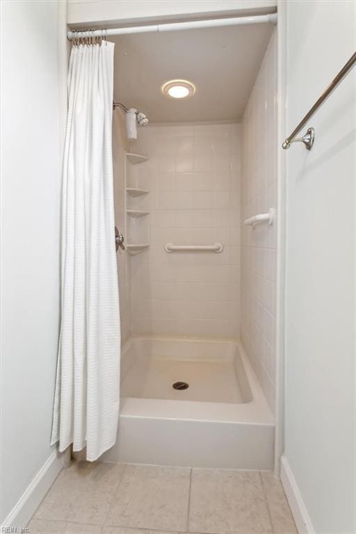 bathroom featuring a tile shower, tile patterned flooring, and baseboards