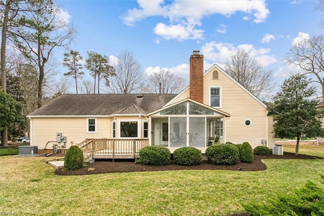 rear view of property featuring a wooden deck, a lawn, a sunroom, and a chimney